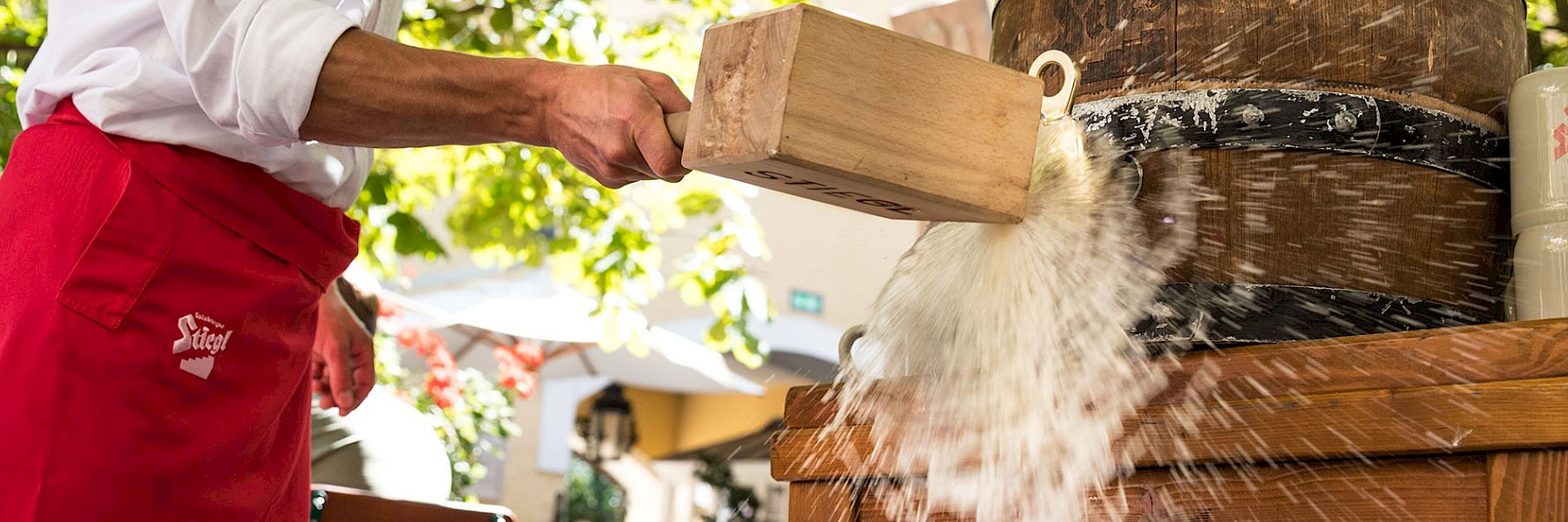 Das Bild zeigt sechs Bierflaschen der Marke „Stiegl Salzburger Goldbräu“ in einem schwarzen Metallzuber, der mitten in einem goldgelben Gerstenfeld steht. Die grünen Flaschen mit roten Etiketten und Kronkorken heben sich kontrastreich vom warmen, natürlichen Hintergrund ab. Die Szenerie verbindet Ursprünglichkeit und Regionalität und verweist auf die natürlichen Zutaten des Bieres. Das Bild vermittelt sommerliche Stimmung, Frische und den Bezug zur traditionellen Braukunst – ideal für Werbung oder Präsentation einer regional verwurzelten Brauerei mit Qualitätsanspruch.